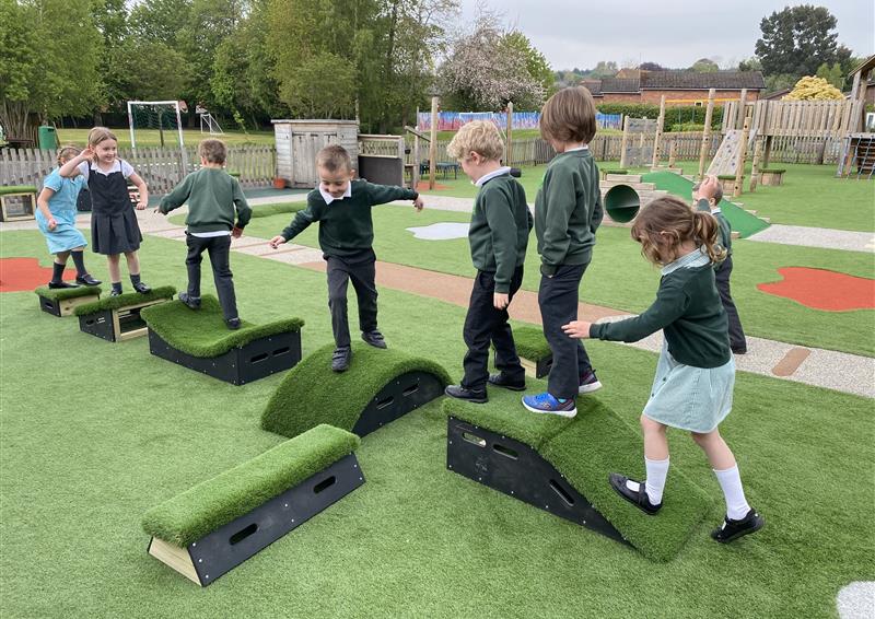 8 blocks from the Get Set, Go! Blocks have been laid out in a cross shape on top of an artificial turf. 8 Children are playing on top of all the different blocks as they travel across them.